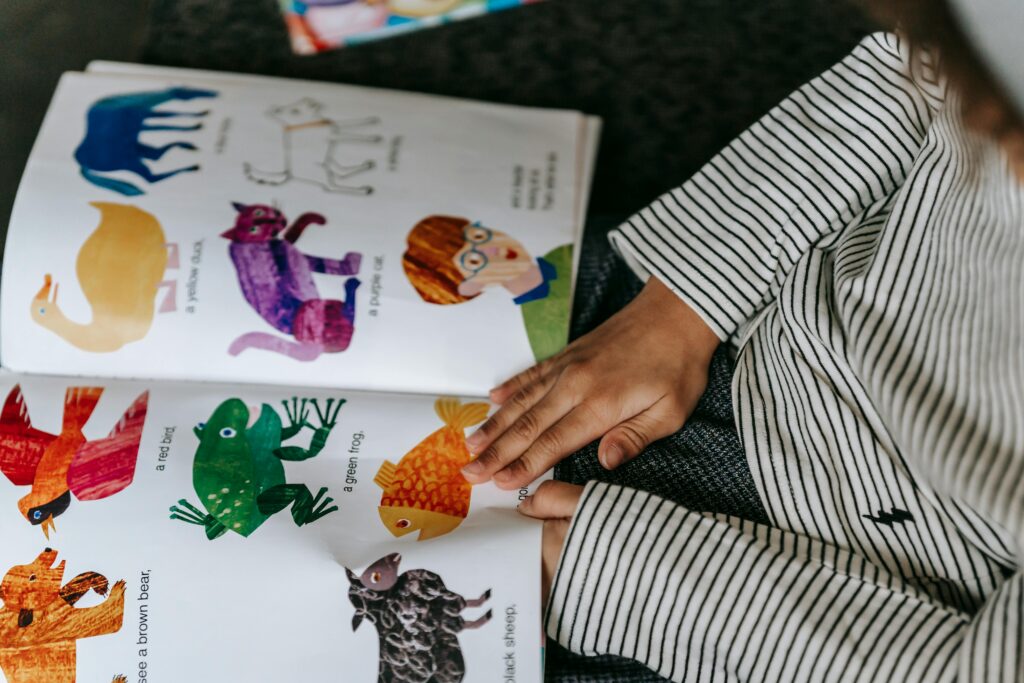 From above of crop anonymous child reading interesting book with colorful pictures of different animals